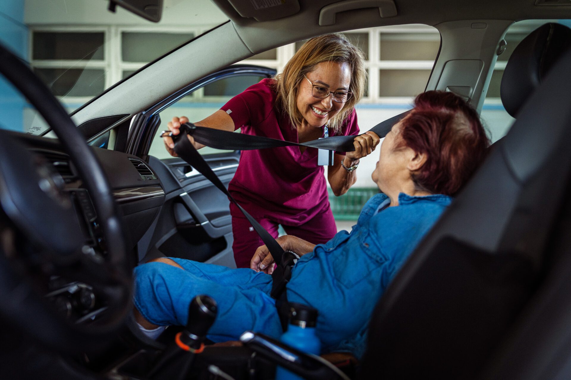 A caregiver offering senior transportation services in the Brookfield area buckles a senior into the passenger seat of a car.