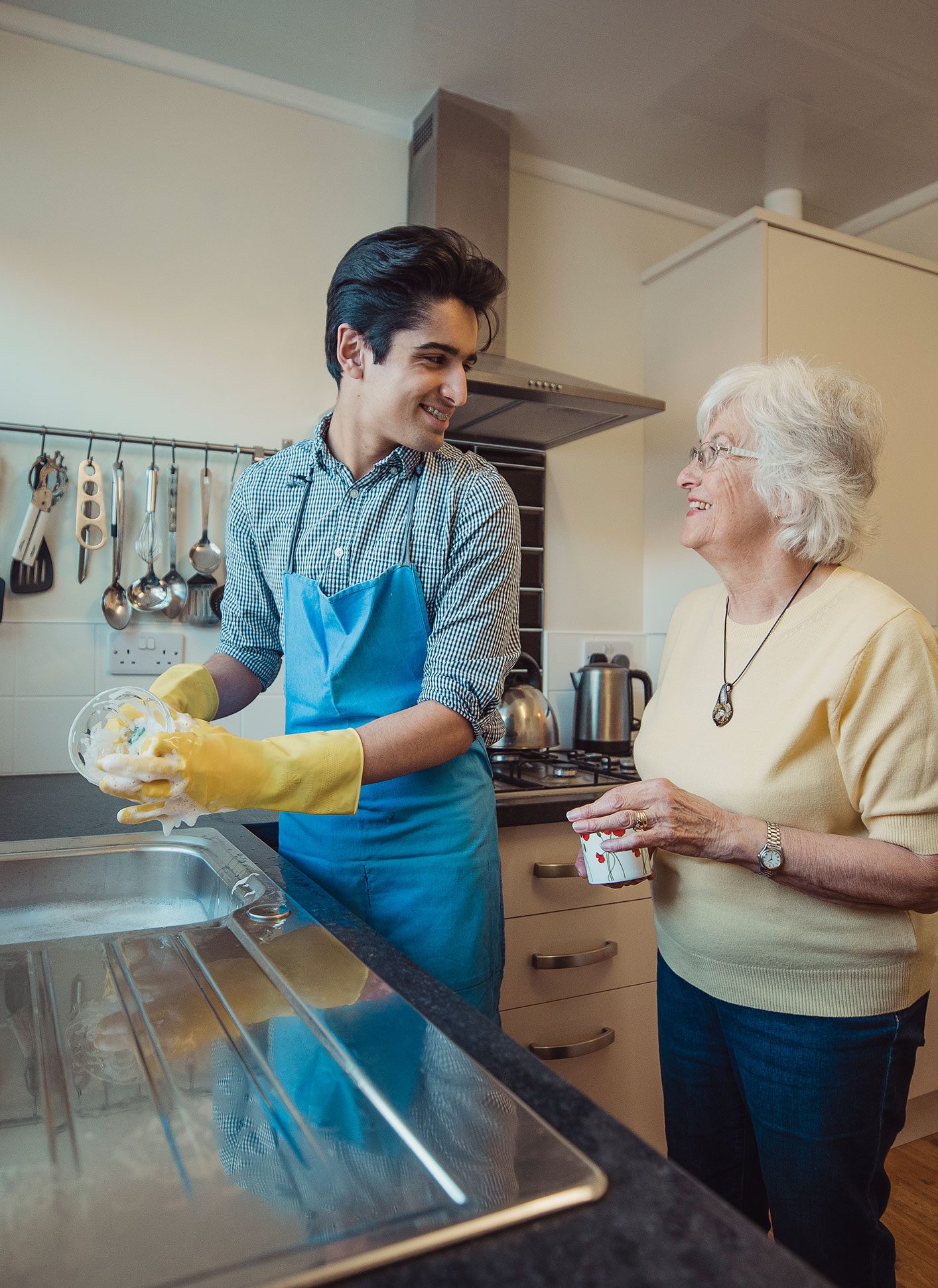 An older woman receiving senior housekeeping services watches her caregiver wash dishes.
