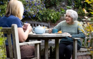 Mature Woman Visiting Lonely Senior Mother In Garden During Lockdown